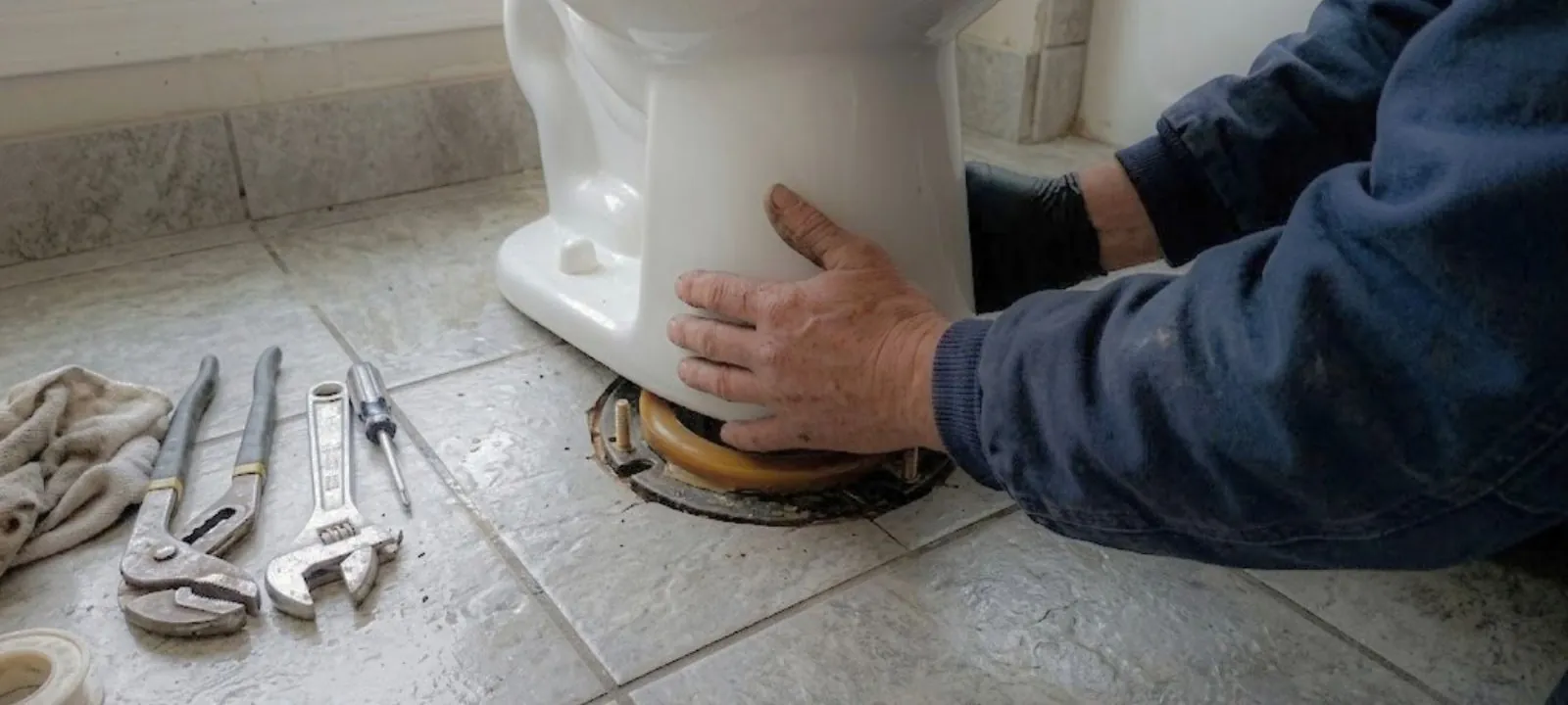 Plumber setting a toilet onto its floor flange with tools beside it