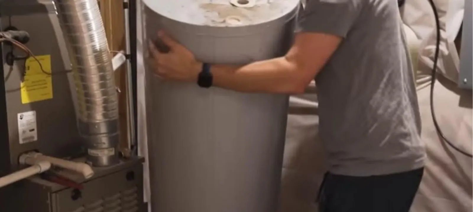 Plumber carrying a new tank water heater into a utility room beside a furnace