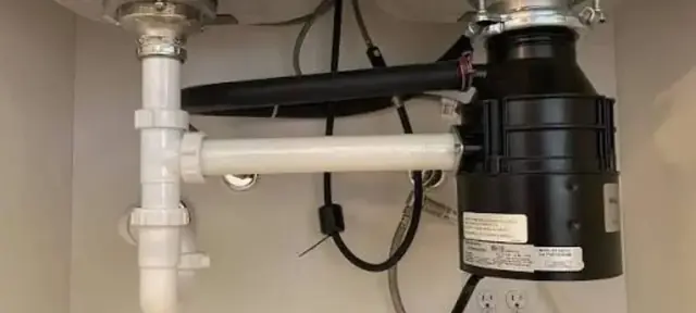 Garbage disposal mounted under a kitchen sink with its drain plumbing