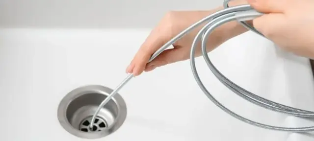 Hands feeding a flexible drain wire into a white sink drain