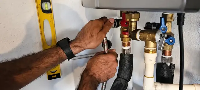 Plumber working on the valves under a wall-mounted tankless water heater